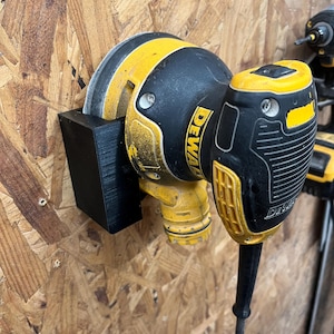 May include: A black and yellow DeWalt power tool is mounted on a wooden surface. The tool is secured in a black holder. The tool has the brand name "DEWALT" printed on it.