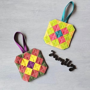 May include: Two colourful, geometric fabric ornaments with hanging loops. One is yellow, pink, and teal, the other is red, yellow, and green. A black wooden word "Family" is also present.