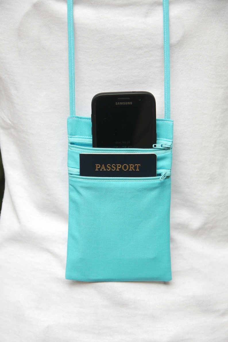 May include: A turquoise zippered pouch with a black Samsung phone and a passport inside. The pouch has a white strap and is worn over the shoulder.