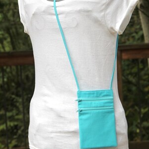 May include: A turquoise zippered pouch with a long strap, worn as a crossbody bag. The pouch has three zippered compartments.