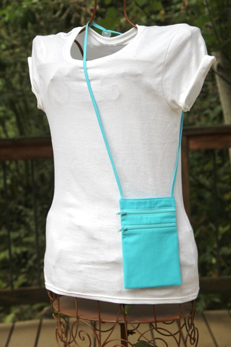 May include: A turquoise zippered pouch with a long strap, worn as a crossbody bag. The pouch has three zippered compartments.