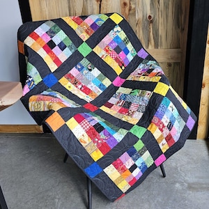 May include: A colorful patchwork quilt with a black background and a diamond pattern. The quilt is made of many different fabrics and colors, including red, yellow, blue, green, and purple.