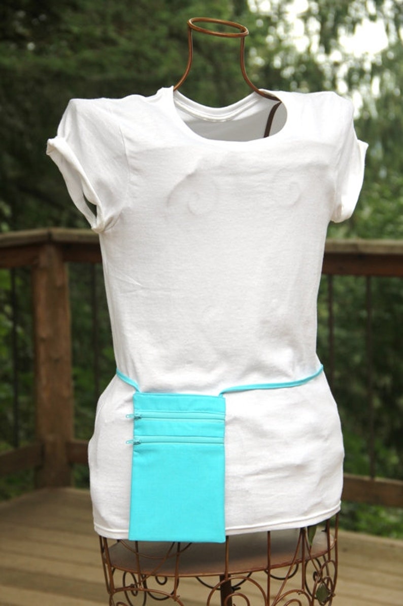 May include: A white t-shirt with a turquoise fabric pouch attached to a belt around the waist.