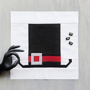 Peut inclure: Un carré de tissu blanc avec un motif de chapeau noir et rouge au centre. Les mots "make life fun" sont écrits sur trois petits carreaux noirs.