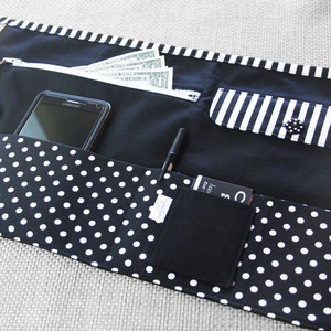 May include: Black and white polka dot fabric apron with multiple pockets. The apron has a zippered pocket, a cell phone pocket, a pen pocket, a small pocket for cards, and a key chain holder.
