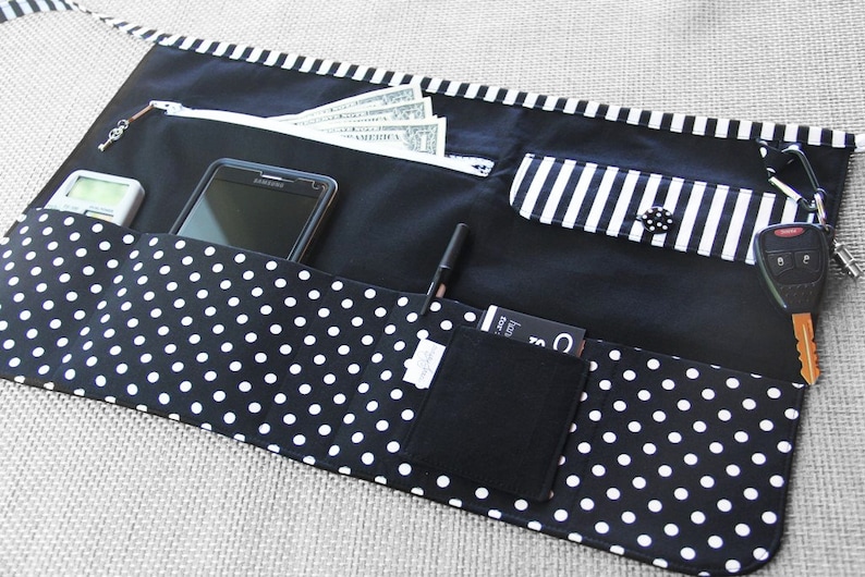 May include: Black and white polka dot fabric apron with multiple pockets. The apron has a zippered pocket, a cell phone pocket, a pen pocket, a small pocket for cards, and a key chain holder.