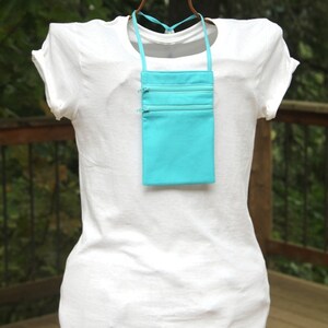 May include: A turquoise zippered pouch with a long strap, worn as a necklace on a white t-shirt.