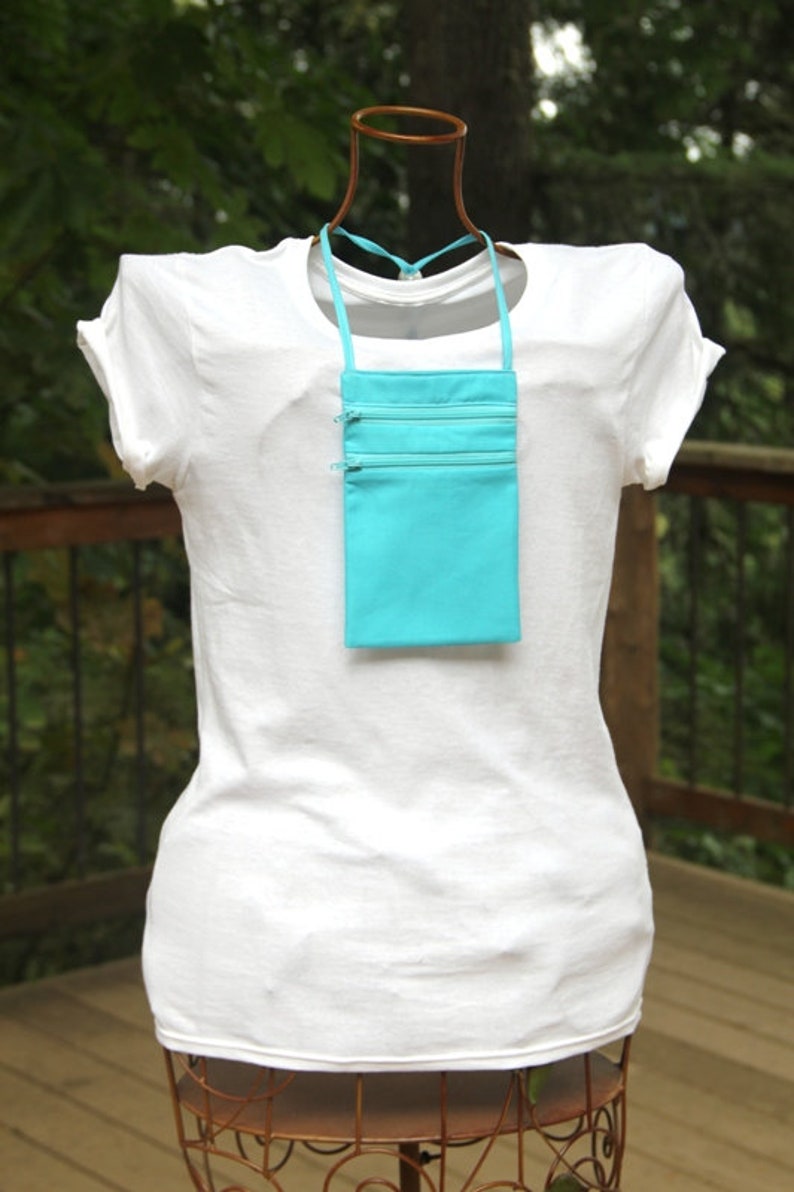May include: A turquoise zippered pouch with a long strap, worn as a necklace on a white t-shirt.
