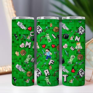 Puede incluir: Tres vasos aislados verdes con un diseño pixelado que presenta personajes, herramientas e iconos del videojuego Minecraft. El diseño incluye corazones, espadas y la palabra CRAFT.