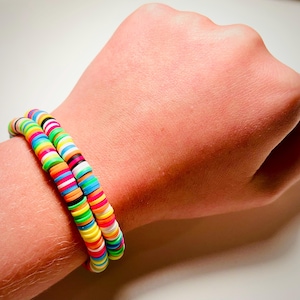 May include: Two colorful beaded bracelets. Each bracelet is made of small, flat, round beads in a variety of bright colors, including red, orange, yellow, green, blue, and purple. The bracelets are stacked on top of each other.