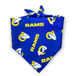 May include: Blue dog bandana with a repeating pattern of the Los Angeles Rams logo and the word "RAMS" in yellow. The bandana is tied at the top.