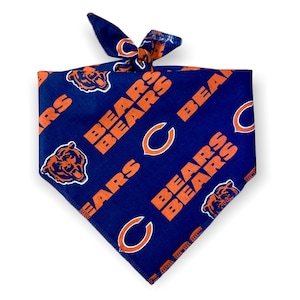 May include: A blue and orange Chicago Bears dog bandana. The bandana features the team's logo, the word "BEARS", and the team's bear head logo. The bandana is tied at the top.
