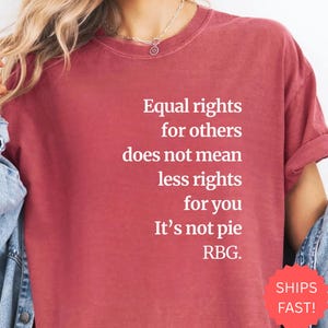 Puede incluir: Camiseta granate con texto blanco: "Igualdad de derechos para los demás no significa menos derechos para ti. No es pastel. RBG." La camiseta tiene cuello redondo y mangas cortas.