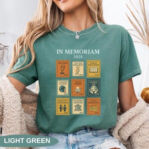 May include: Light green t-shirt with the text "IN MEMORIAM 2025" and postage stamp-style graphics. The stamps depict themes like free press, vaccine research, climate action, and global aid. The shirt also has the text "LIGHT GREEN" at the bottom.