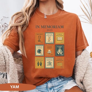 May include: Burnt orange t-shirt with the text "IN MEMORIAM 2025" and postage stamp-style graphics. Stamps include images of a microphone, DNA, an open book, a globe, and a radio. The shirt also has the word "YAM" at the bottom.