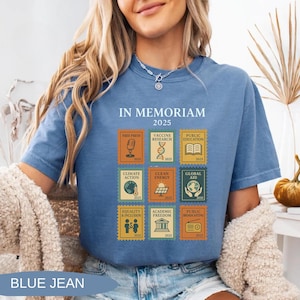 May include: Blue jean-colored t-shirt with the text "IN MEMORIAM 2025". The shirt features nine postage stamp-style graphics with themes like "Free Press", "Vaccine Research", and "Public Education". The shirt is made of a soft material.