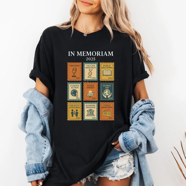 May include: Black t-shirt with the text "IN MEMORIAM 2025" and postage stamp-style graphics. The stamps feature icons and text related to social and environmental issues, including "FREE PRESS" and "CLIMATE ACTION."