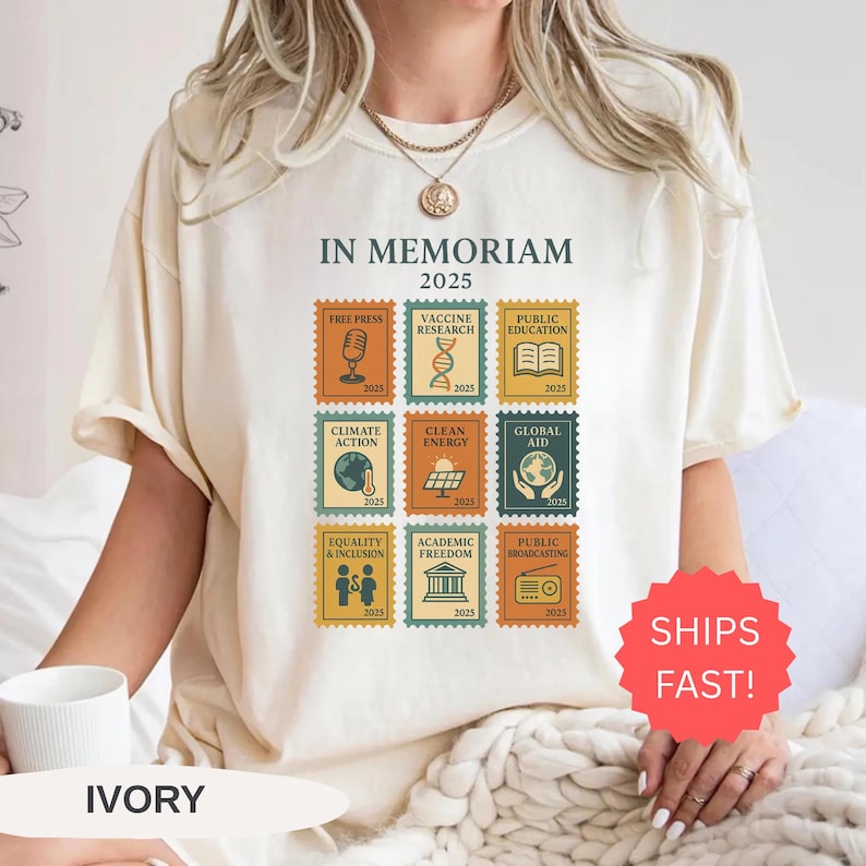 May include: Ivory-colored t-shirt featuring the text "IN MEMORIAM 2025" above nine postage stamp-style graphics. Each graphic represents a different topic, including "Free Press," "Vaccine Research," and "Public Education."