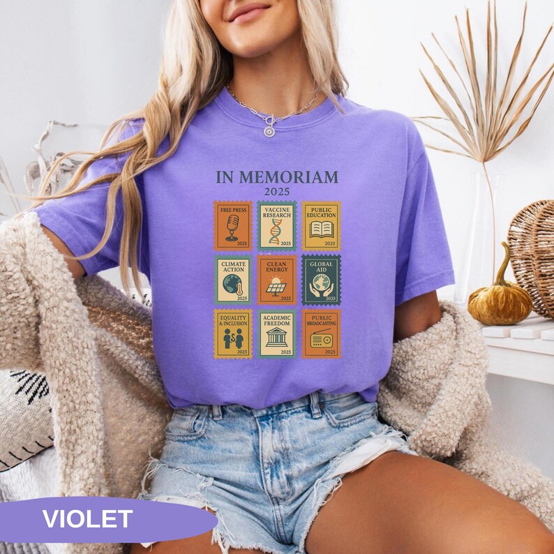 May include: Violet-colored t-shirt with the text "IN MEMORIAM 2025" and postage stamp-style graphics. The stamps depict themes like free press, vaccine research, and climate action. The word "VIOLET" is at the bottom of the image.