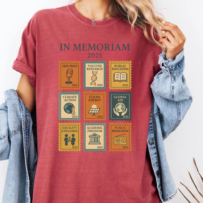 May include: Burgundy-colored t-shirt with the text "IN MEMORIAM 2025" and postage stamp-style graphics. The stamps depict themes like "Free Press," "Climate Action," and "Equality & Inclusion." Each stamp includes the year 2025.