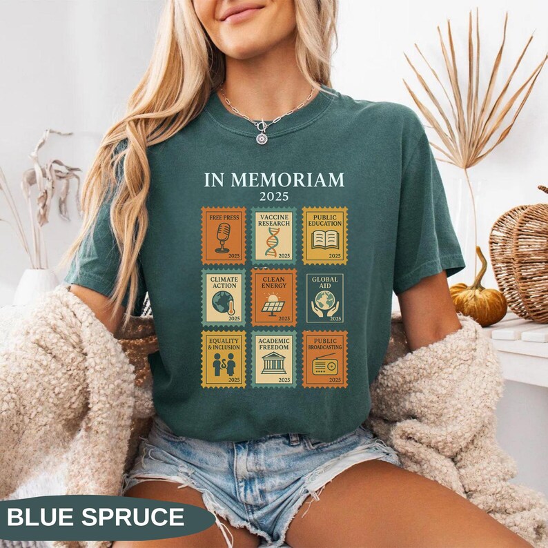 May include: Blue spruce t-shirt with a graphic of postage stamps featuring the words "IN MEMORIAM 2025." Stamps include "Free Press," "Vaccine Research," "Public Education," "Climate Action," "Clean Energy," "Global Aid," "Equality & Inclusion," "Academic Freedom," and "Public Broadcasting."