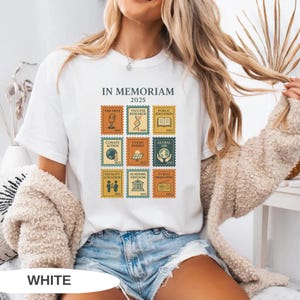 May include: White t-shirt with the text "IN MEMORIAM 2025" and postage stamp-style graphics. The stamps feature icons related to free press, vaccine research, public education, climate action, clean energy, and global aid.
