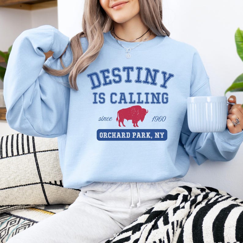 May include: Light blue sweatshirt with the text "DESTINY IS CALLING" above a red buffalo graphic and the words "since 1960 ORCHARD PARK, NY". The sweatshirt is a crew neck style.