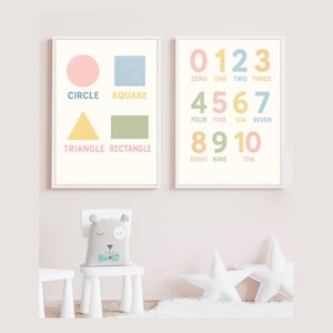 May include: Two framed educational prints with pastel shapes and numbers. One print displays a pink circle, blue square, yellow triangle, and green rectangle with their names. The other shows numbers 0-10 with their written forms.