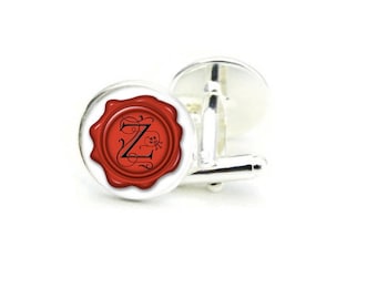 May include: Silver cufflinks with a red wax seal design. The seal features a black letter "Z" in an ornate script. The cufflinks have a shiny, polished finish, perfect for formal wear or adding a touch of elegance to any outfit.