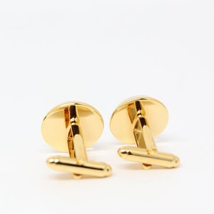 May include: A pair of gold cufflinks with a round, smooth surface. The cufflinks have a simple, classic design.