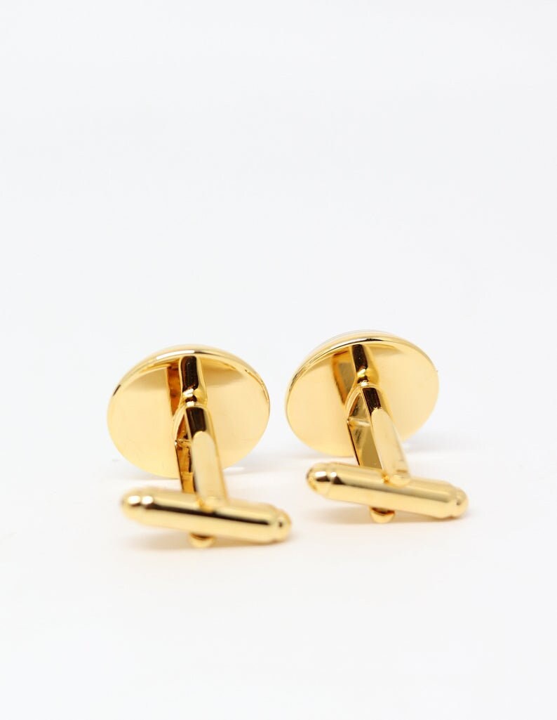 May include: A pair of gold cufflinks with a round, smooth surface. The cufflinks have a simple, classic design.
