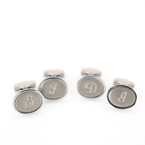 May include: Silver-toned oval cufflinks with engraved initials. The cufflinks have a brushed metal finish and a polished silver border. The initials "S", "F", "D", and "g" are displayed on the face of each cufflink. The cufflinks are presented on a white background.