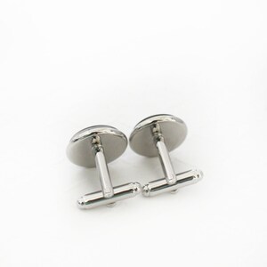 May include: A pair of silver cufflinks with a dark, possibly black, oval-shaped face. The cufflinks have a shiny, polished finish and a classic design, suitable for formal wear. The cufflinks are set against a white background.