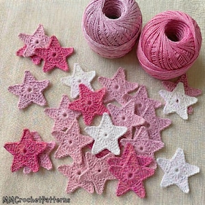 Puede incluir: Dos ovillos de hilo rosa situados sobre una colección de pequeñas estrellas de ganchillo de cinco puntas en varios tonos de rosa, magenta y blanco. El texto "MMCrochetPatterns" está impreso en la esquina inferior izquierda.