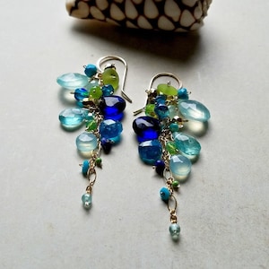 May include: A pair of long, dangling earrings with a cascade of blue, green, and white gemstones. The earrings are made with gold chain and feature a variety of shapes and sizes of stones.