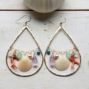 Puede incluir: Pendientes de oro en forma de lágrima con una variedad de encantos que incluyen conchas marinas, coral, turquesa, amatista y perlas.