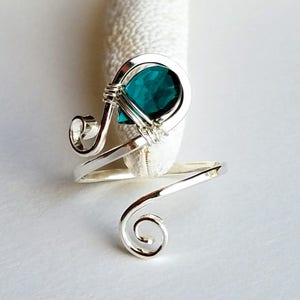 May include: A silver wire ring with a teal gemstone set in a swirl design.