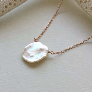 May include: A delicate rose gold chain necklace with a large, irregular, white freshwater pearl pendant.