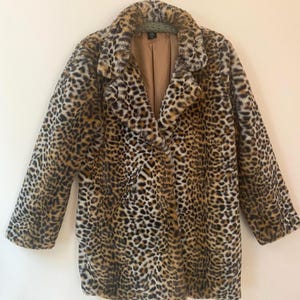 May include: A leopard print faux fur coat with a notched collar and a button closure. The coat is brown, black, and tan, and hangs on a hanger against a neutral background. The coat has a soft, plush texture.