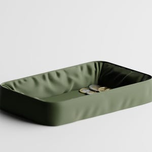 Puede incluir: Una bandeja rectangular verde oliva con un interior texturizado. Varias monedas son visibles dentro de la bandeja. La bandeja tiene esquinas redondeadas y un exterior liso, adecuada para organizar objetos pequeños.