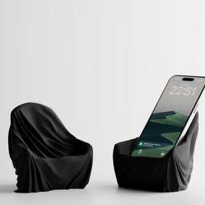 Peut inclure: Deux supports de téléphone noirs en forme de chaise abstraite. L'un est vide, l'autre contient un smartphone affichant un paysage vert et l'heure 22:51. Les supports sont drapés d'un tissu, créant un design artistique unique.