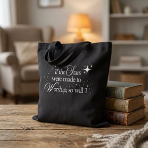 May include: A black tote bag featuring white printed text that reads, "If the Stars were made to Worship, so will I," accompanied by small star graphics. The bag has two fabric handles and is positioned next to a stack of three vintage books.