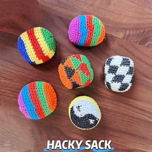 May include: A selection of colourful hacky sacks, each with a unique design. The sacks feature various patterns, including stripes, a yin-yang symbol, and a football design. The text "HACKY SACK" is displayed at the bottom.
