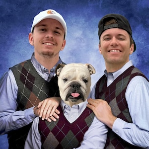 Puede incluir: Tres personas, dos hombres y un bulldog, llevan chalecos de rombos sobre camisas abotonadas de color azul claro. Un hombre lleva una gorra de béisbol blanca y el otro una gorra de béisbol negra. El bulldog tiene la lengua fuera.