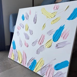 May include: A rectangular white canvas featuring thick, textured impasto paint strokes in pastel shades of light blue, soft pink, pale yellow, and lavender. The paint is applied in distinct, raised dabs and smears across the surface.
