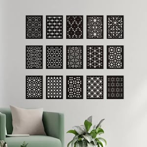 Può includere: Un moderno soggiorno con una poltrona verde chiaro, un tavolino in legno e una lampada da terra. La parete presenta una collezione di 15 pannelli decorativi neri con intricati motivi geometrici, creando un punto focale elegante e artistico.