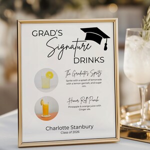 May include: A gold-framed sign titled Grad's Signature Drinks with a graduation cap icon. It lists The Graduate's Spritz and Honor Roll Punch with images of each drink. The bottom text reads Charlotte Stanbury Class of 2026 in black lettering.