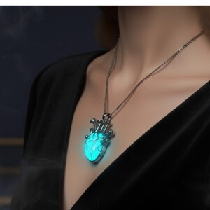 Puede incluir: Un collar plateado con un colgante en forma de coraz&oacute;n turquesa brillante. El colgante en forma de coraz&oacute;n tiene detalles intrincados y cuelga de una delicada cadena. El collar se lleva sobre una parte superior negra.
