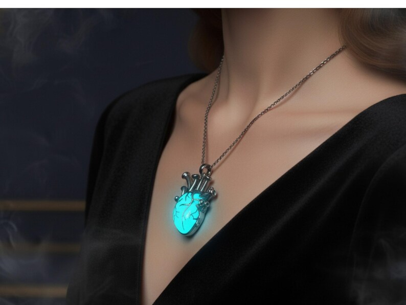 Puede incluir: Un collar plateado con un colgante en forma de coraz&oacute;n turquesa brillante. El colgante en forma de coraz&oacute;n tiene detalles intrincados y cuelga de una delicada cadena. El collar se lleva sobre una parte superior negra.