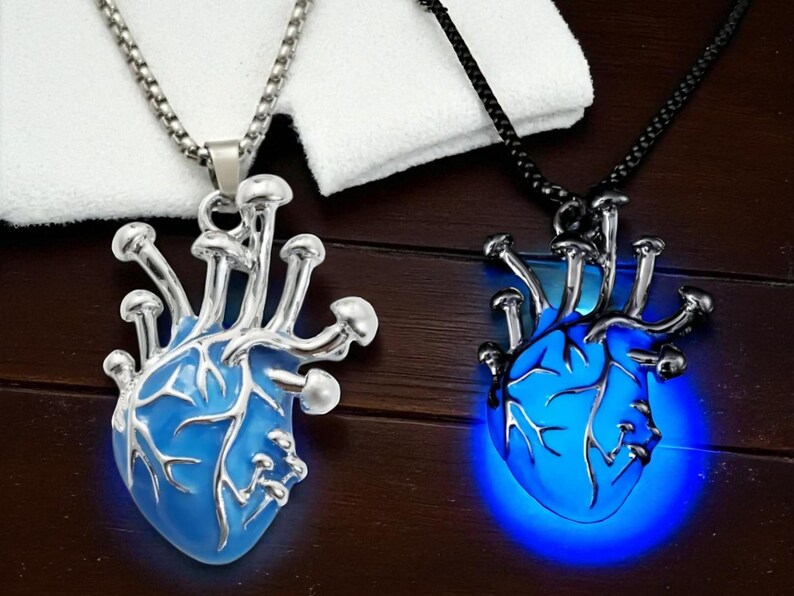 Puede incluir: Dos colgantes en forma de coraz&oacute;n con detalles de hongos. Uno es plateado con un coraz&oacute;n azul, el otro es negro con un coraz&oacute;n azul brillante. Ambos est&aacute;n en cadenas, mostrando un dise&ntilde;o &uacute;nico de inspiraci&oacute;n g&oacute;tica.